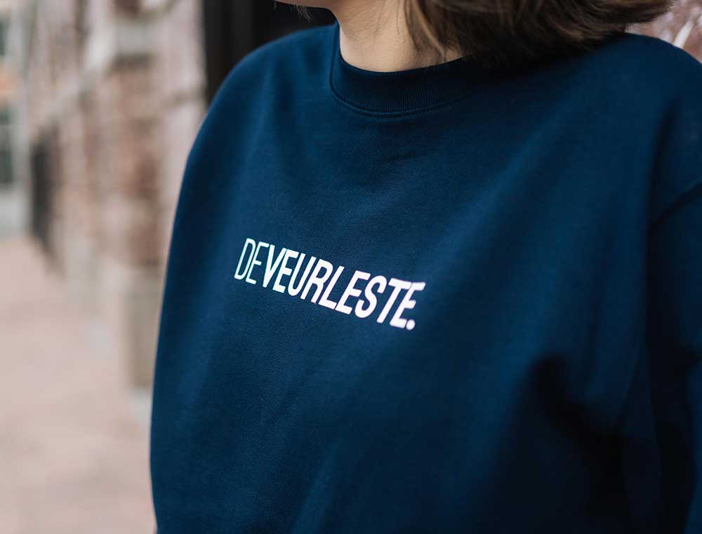 Vrouw met donkerblauwe sweater met opdruk DEVEURLESTE.