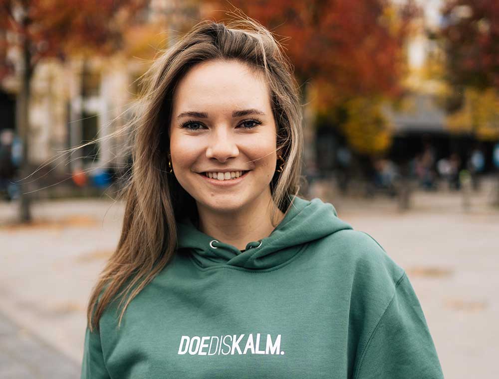 Vrouw met een groene sweater met opdruk DOEDISKALM.