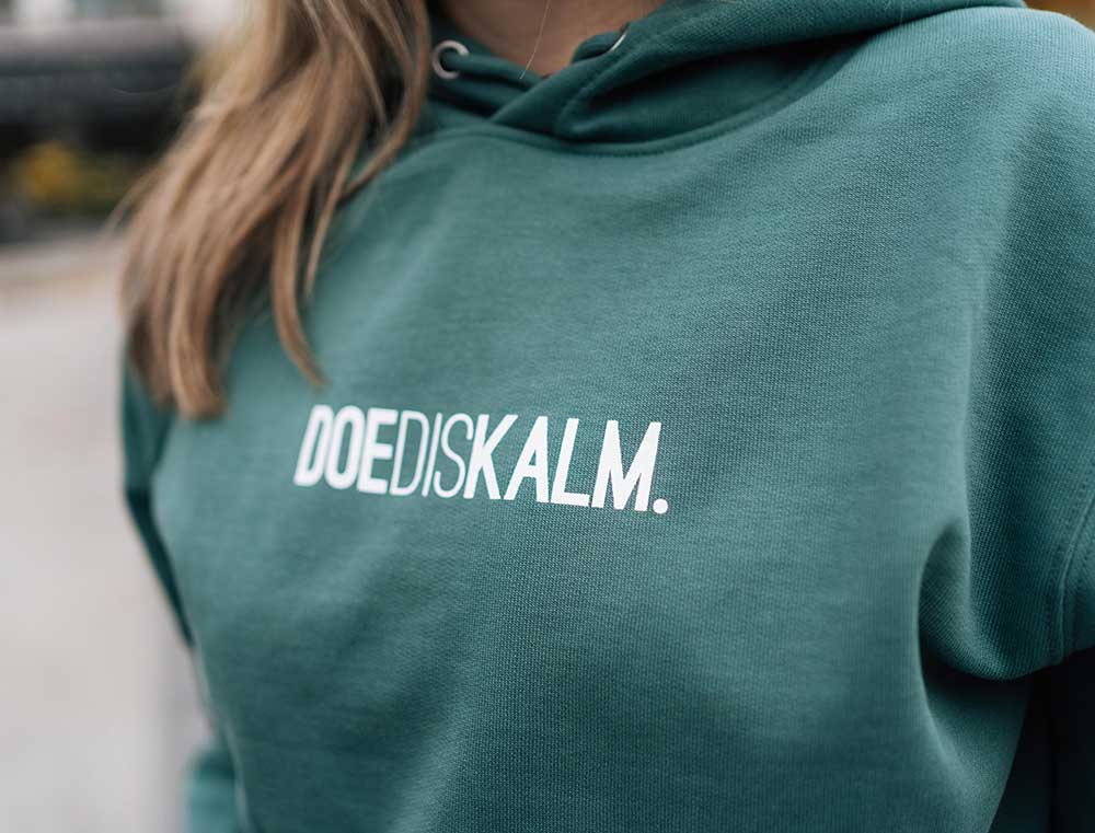 Vrouw met een groene sweater met opdruk DOEDISKALM.