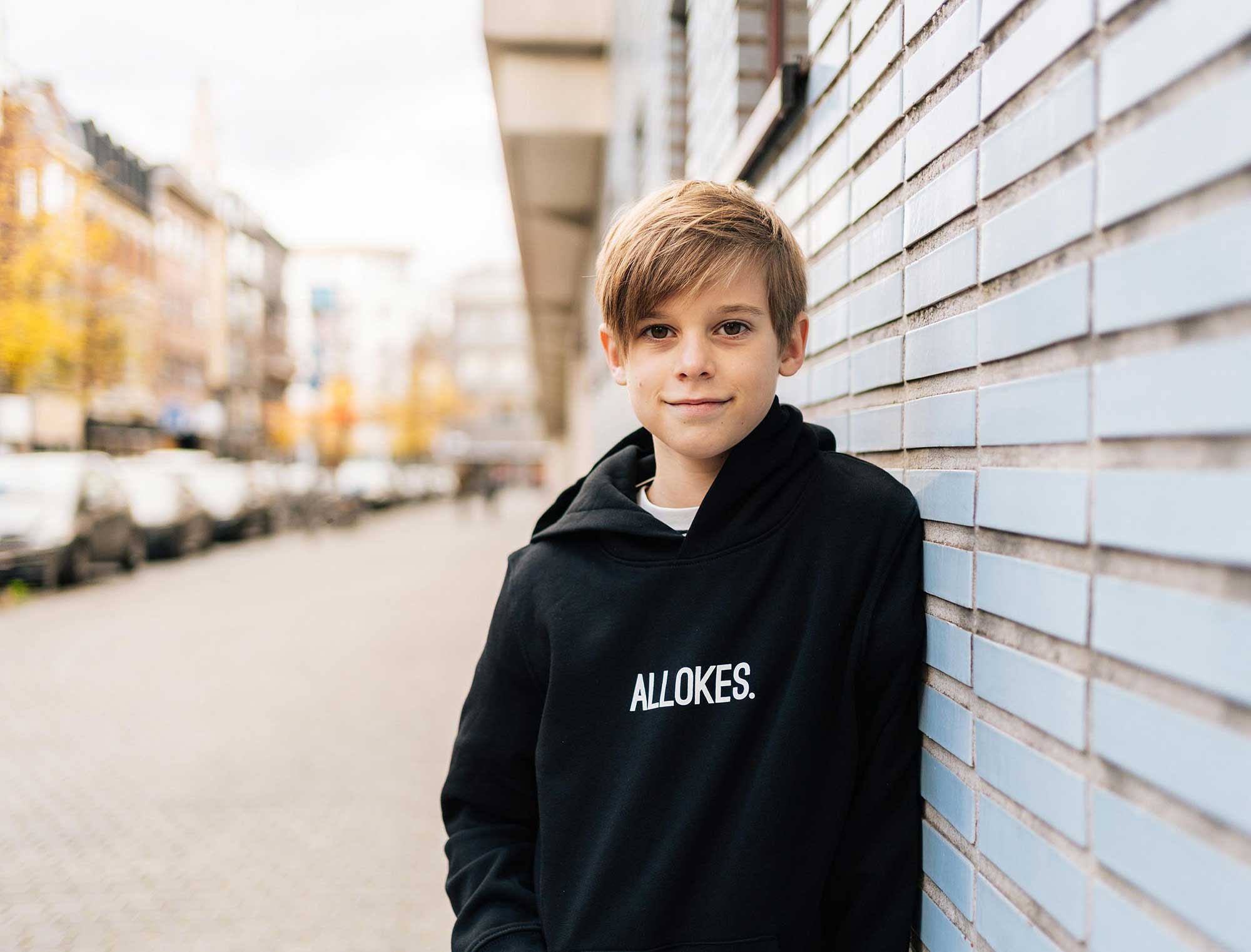 Jongen met een zwarte hoodie voor kinderen met opdruk 'ALLOKES.'